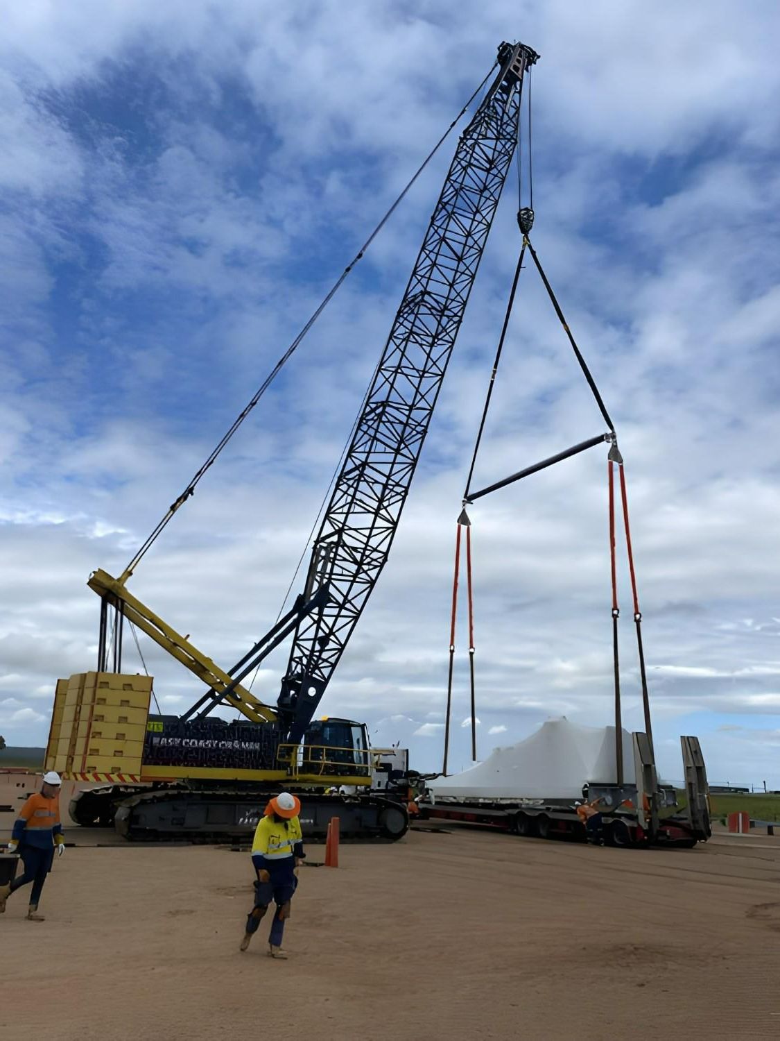 Crane Lifting a Large Object on a Flatbed Trailer; Workers in Safety Gear Nearby, Under Cloudy Sky — East Coast Cranes in Ormeau, QLD