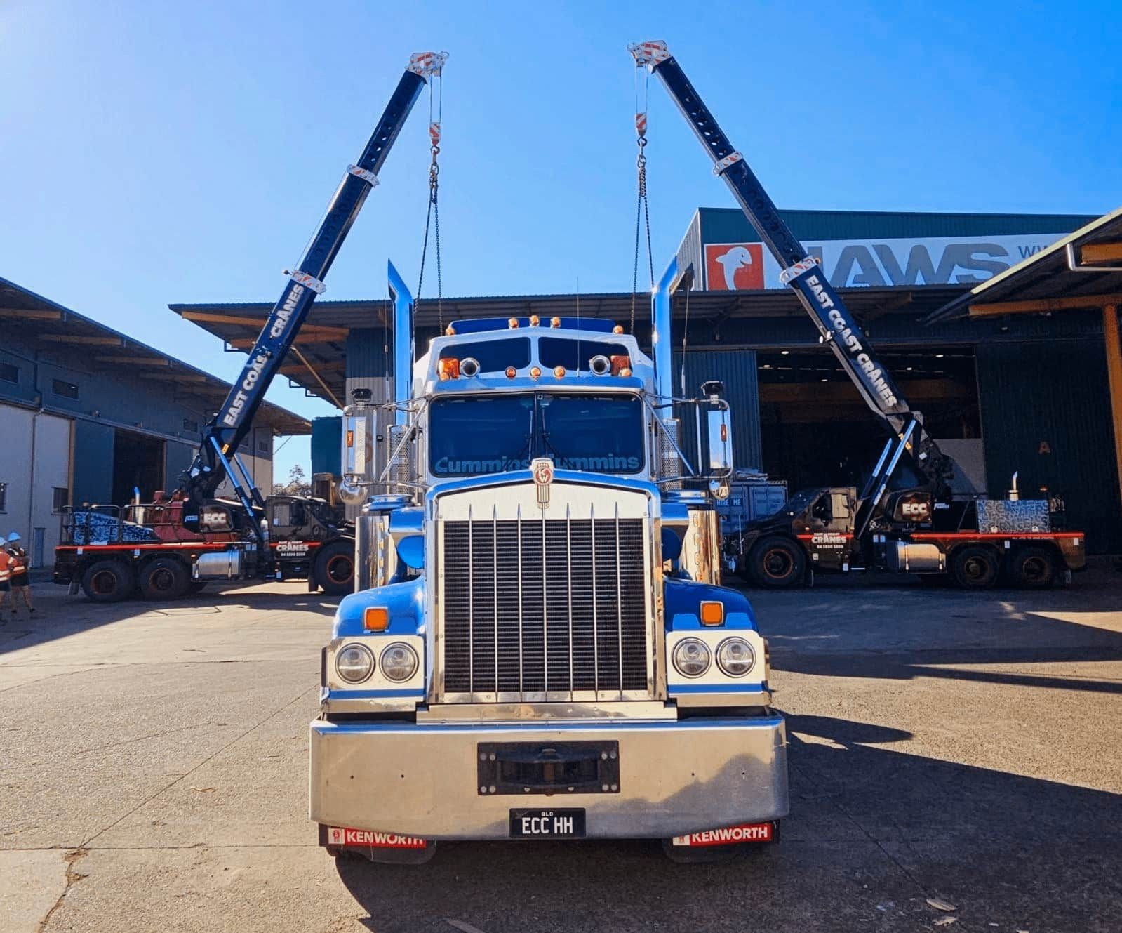Blue Semi-truck With Two Cranes in Front of a Warehouse on a Sunny Day — East Coast Cranes in Newcastle, NSW