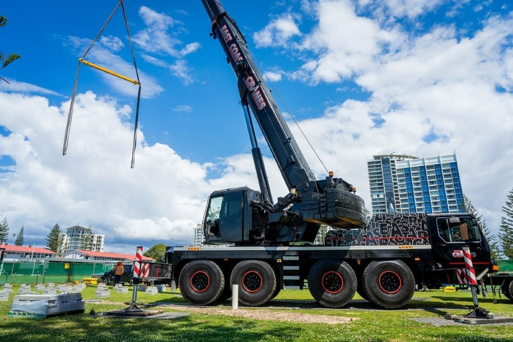 Black Crane Lifting an Object Under a Cloudy Blue Sky. Construction Site Visible in the Background — East Coast Cranes in Ormeau, QLD