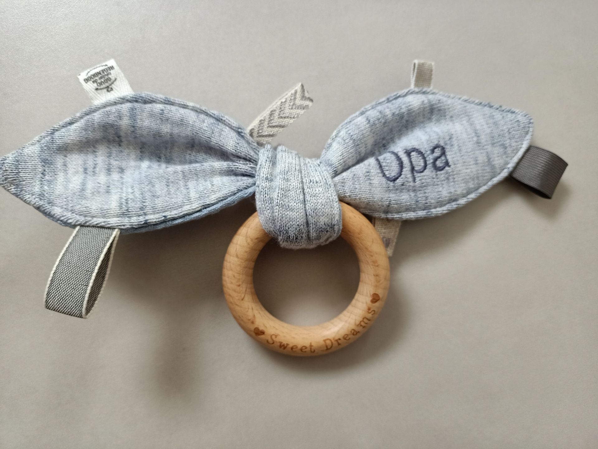 Grijze stoffen babyrammelaar met een houten ring en kleding van overledene op een witte achtergrond