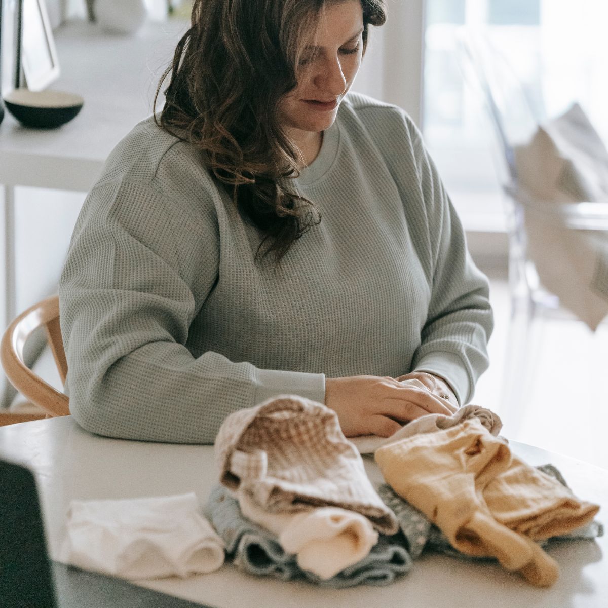 Een vrouw vouwt kleren op aan een tafel in een lichte kamer met stapels neutraal gekleurde kleding.