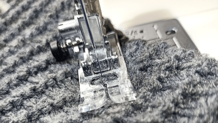 Een close-up van een naaimachine die een stuk gebreide stof aan het naaien is.