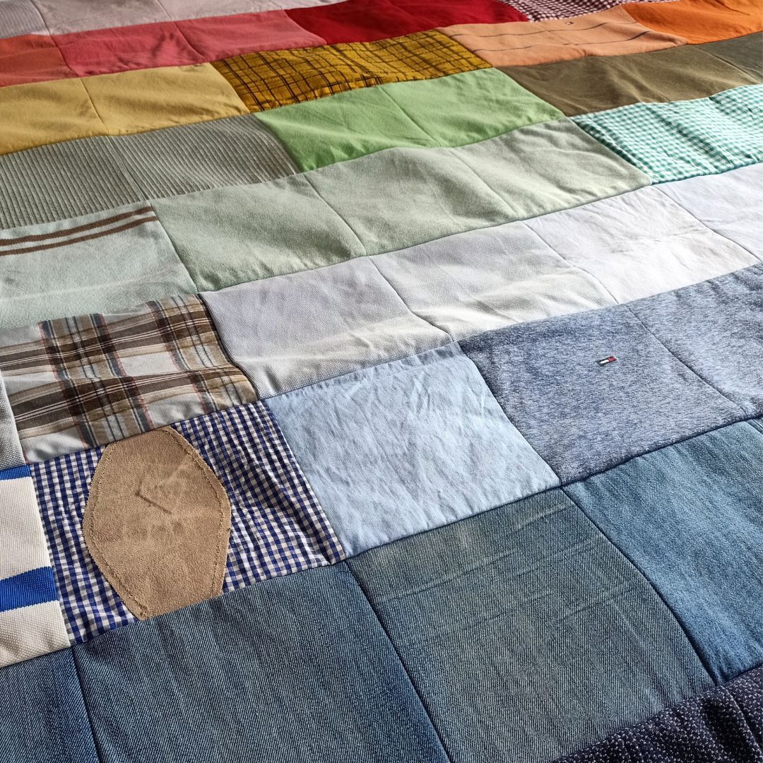 Op een bed ligt een quilt gemaakt van oude overhemden.