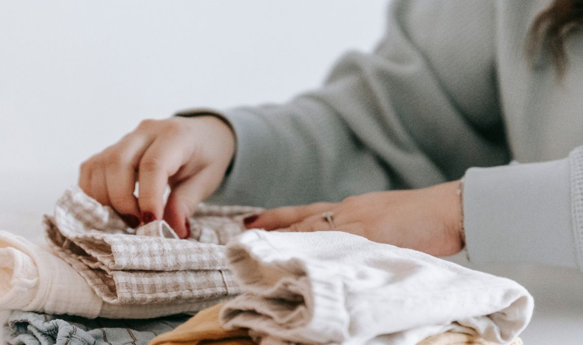 Handen vouwen beige en witte kleding  op een tafel.