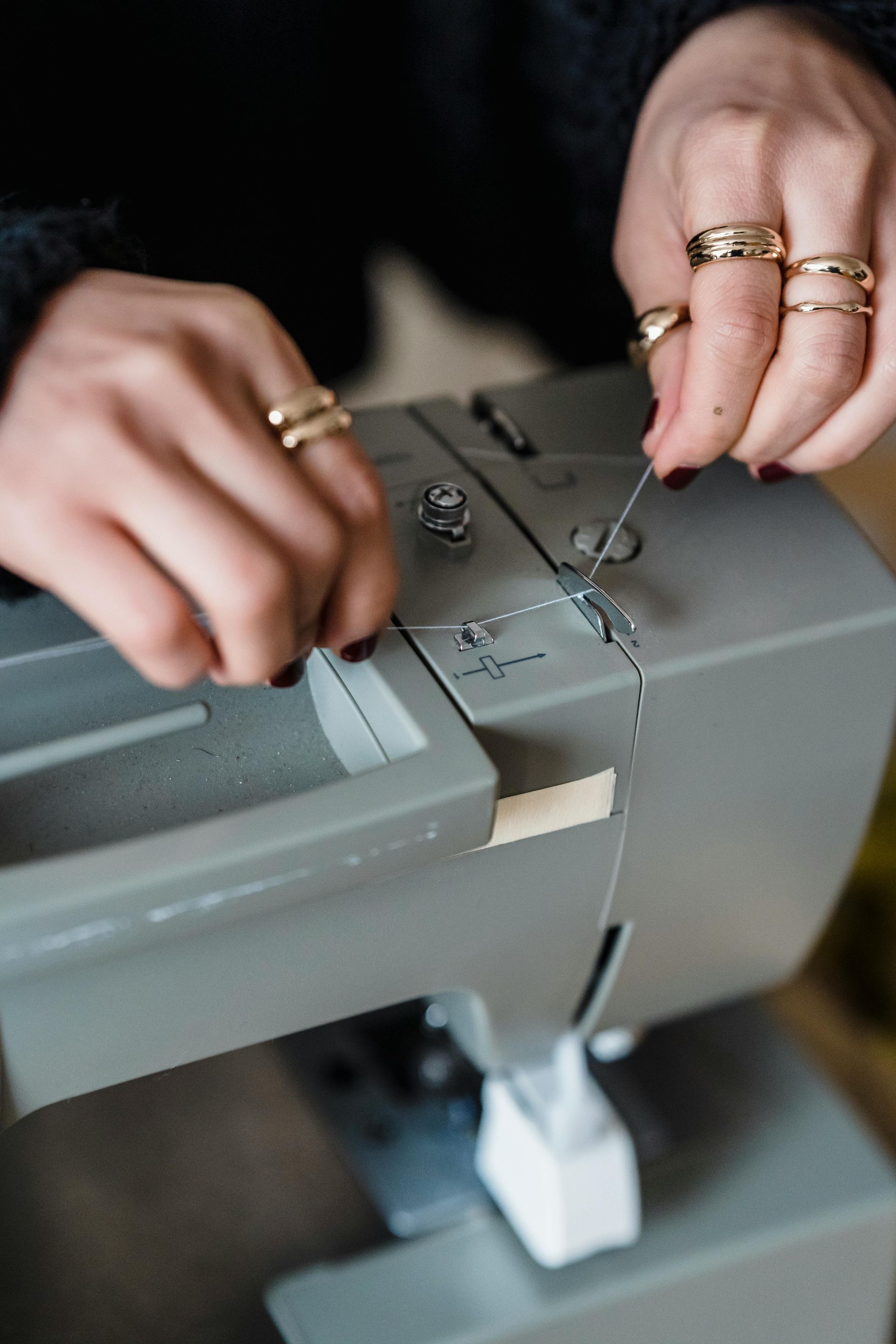 Handen rijgen een grijze naaimachine in met zwart garen.