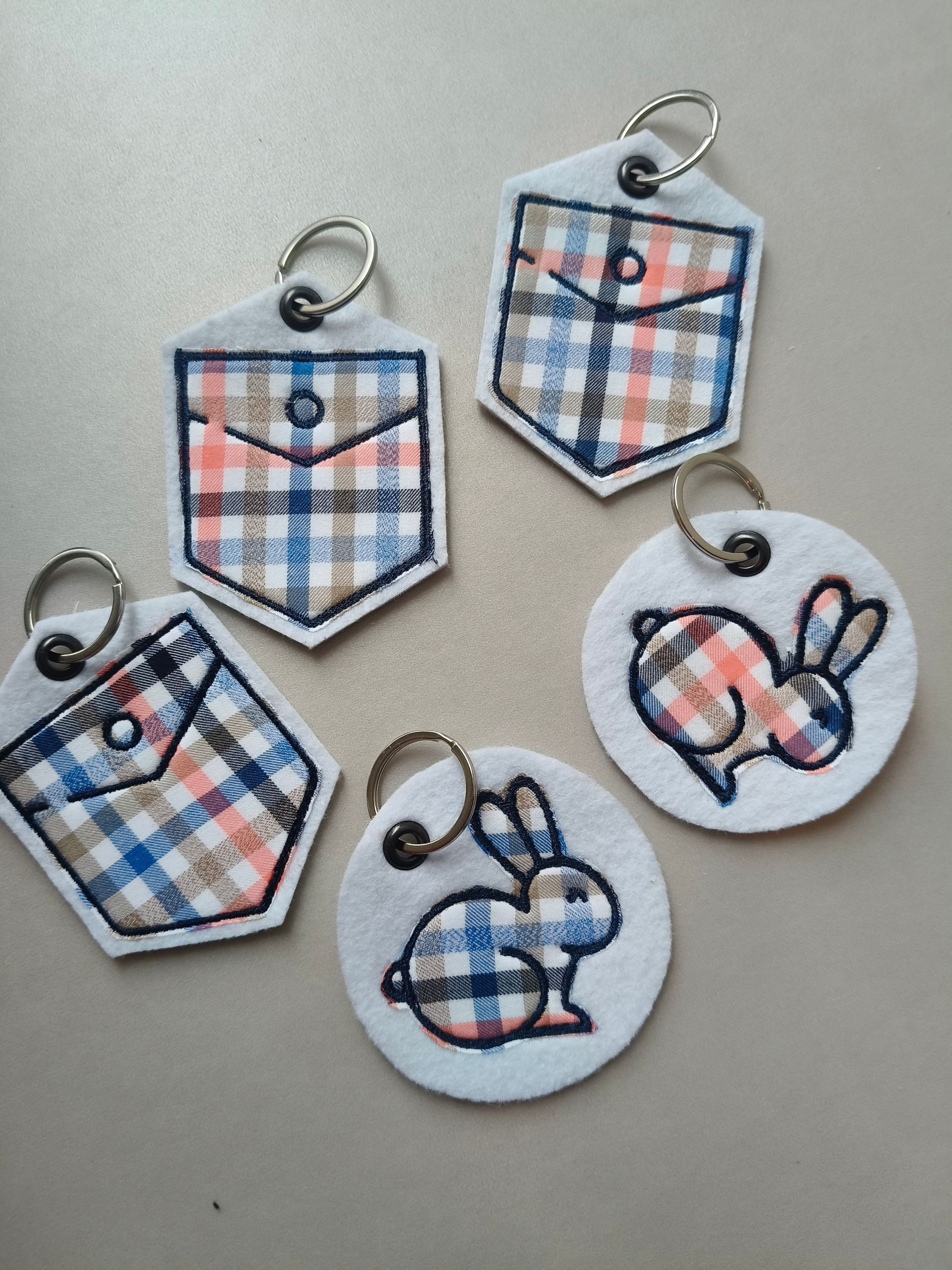 Vijf geruite schildvormige bedeltjes en twee witte konijntjesbedeltjes op een beige ondergrond.