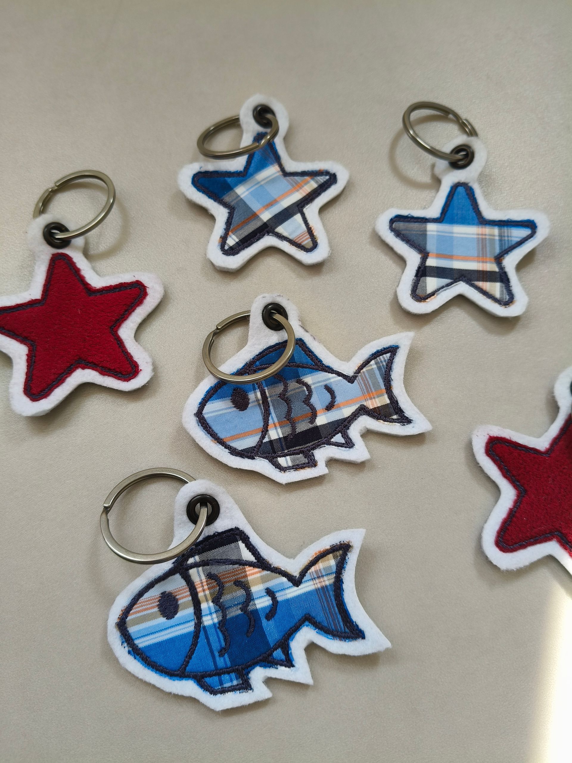 Diverse sleutelhangers met sterren en vissen in blauwe, witte en rode tinten op een lichte ondergrond.