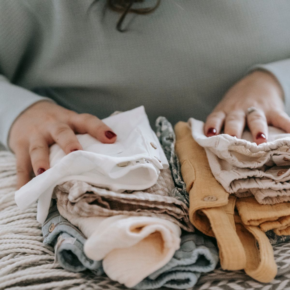 Handen vouwen stapels kleding op een tafel, waaronder witte, beige en grijze kleding.