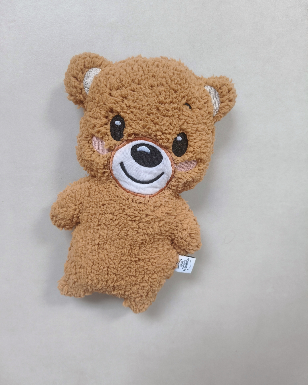Bruine pluche teddybeer gemaakt van dierbare kleding , liggend op een lichtgrijze ondergrond