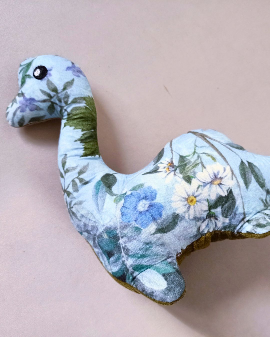 Blauwe pluche dinosaurus met bloemenprint op een lichtroze achtergrond gemaakt van dierbare kleding