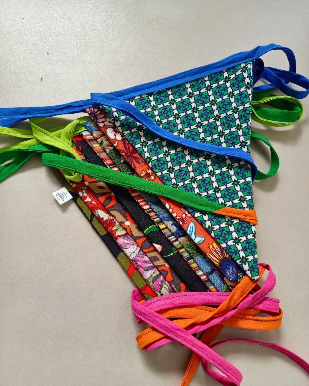 Kleurrijke vlaggenlijn van kleding met blauwe, groene, oranje, roze en patroonvlakken op een grijze achtergrond.