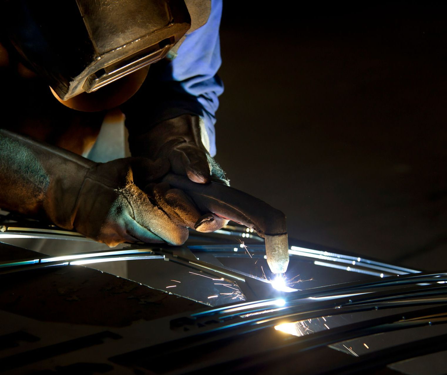 A man is welding a piece of metal in a dark room.
