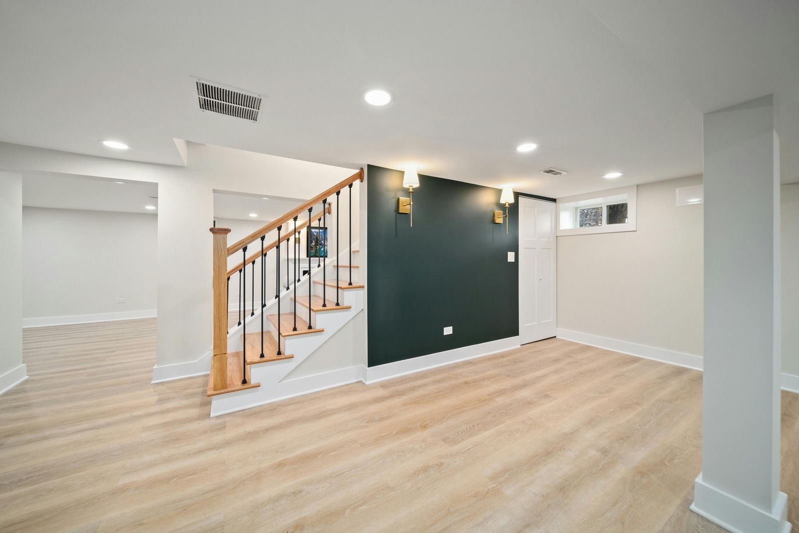 Interior of a finished basement with staircase, wood-look flooring, and dark green accent wall with sconces.