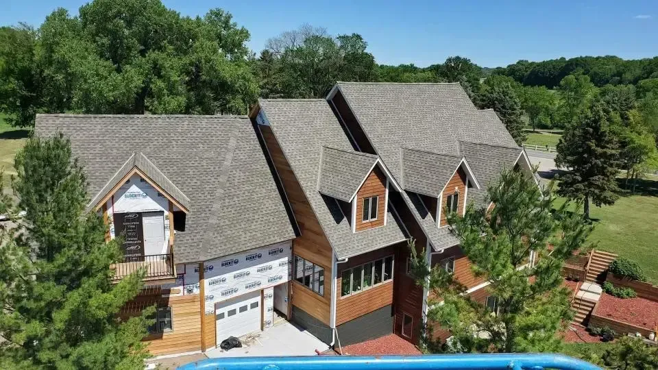 A gray house with large windows, a wooden deck, and a body of water in the background.