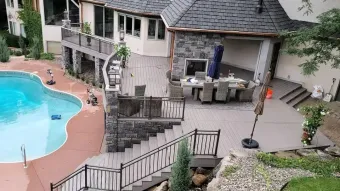A multi-level outdoor area with a pool, patio, dining table, and stone walls.