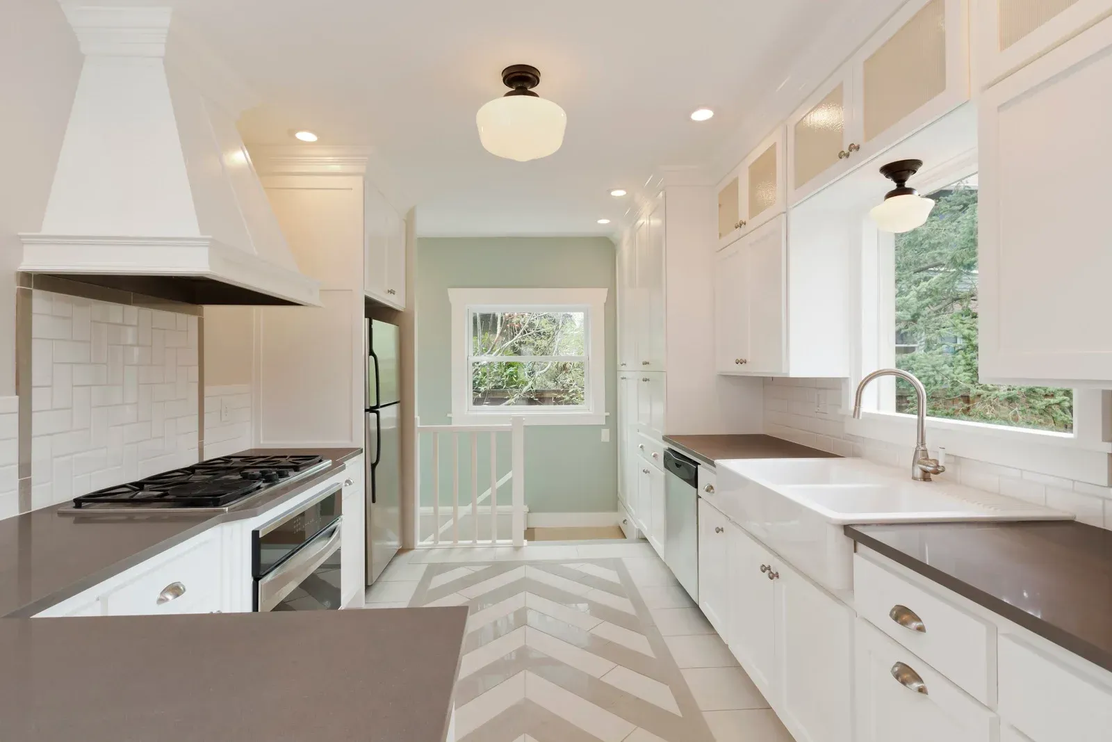 White kitchen with dark countertops, stove, and herringbone floor. A window looks out to greenery.