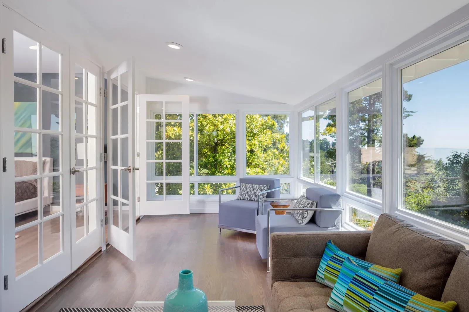 Sunroom with French doors, large windows, and seating, offering a scenic outdoor view.