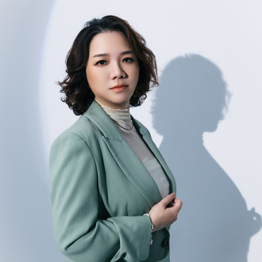 身穿薄荷綠西裝外套的女子站在淺色牆壁前，投下柔和的陰影，表情平靜。