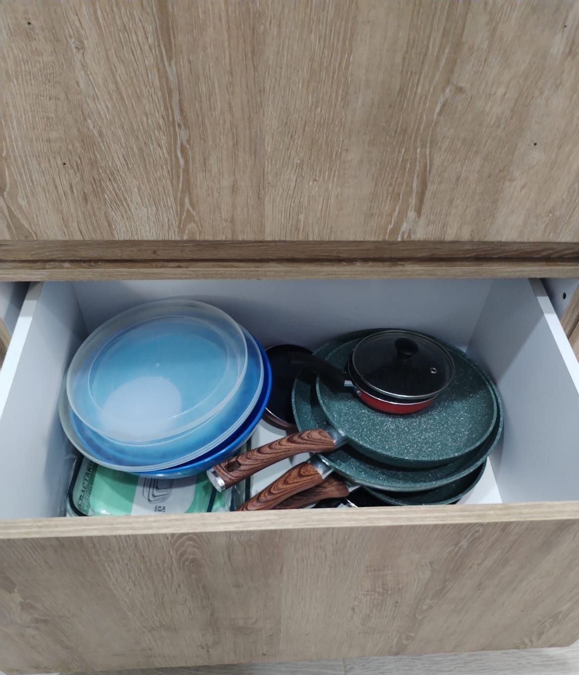 Un cajón de madera lleno de ollas, sartenes y tapas.