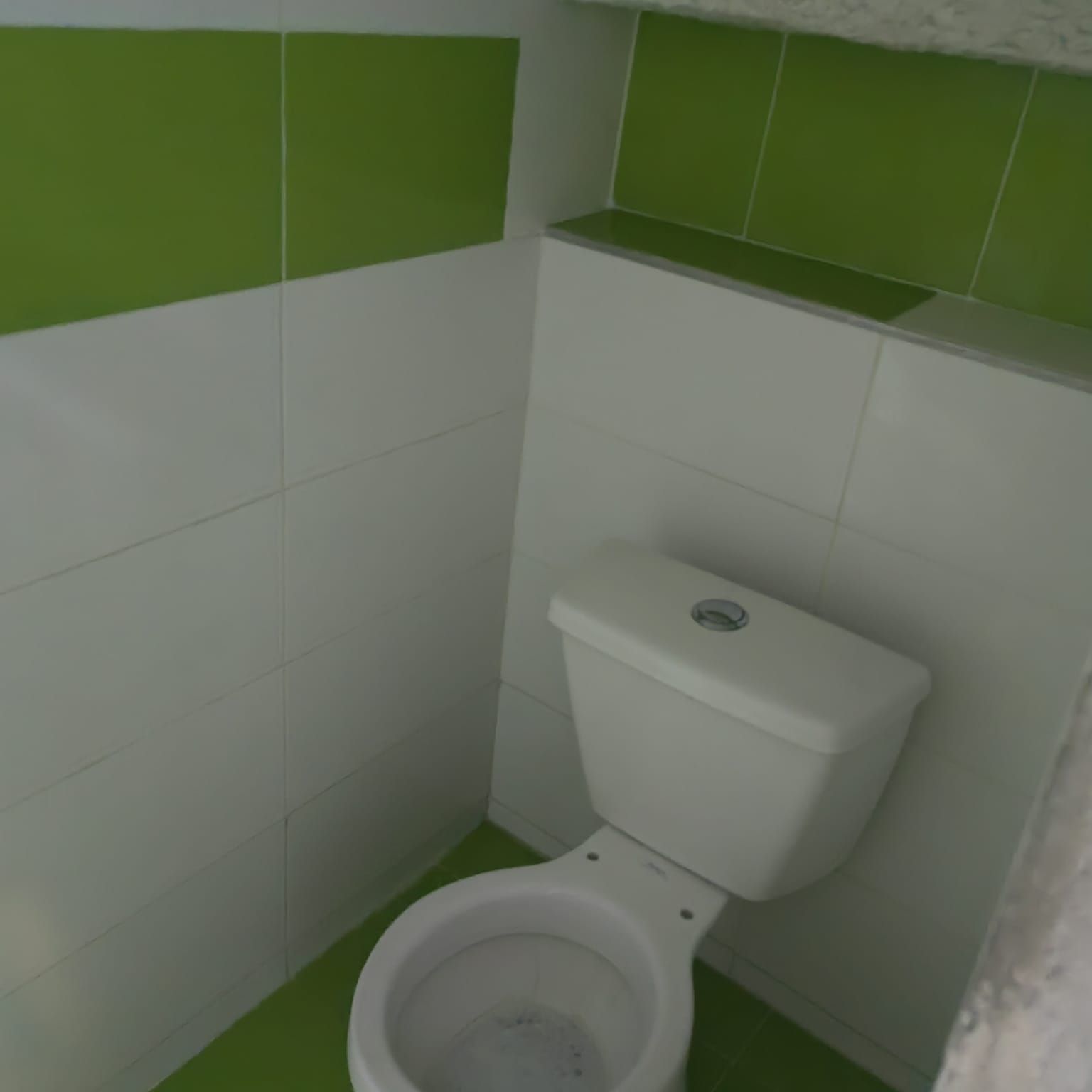 Un inodoro en un baño con azulejos verdes y blancos.