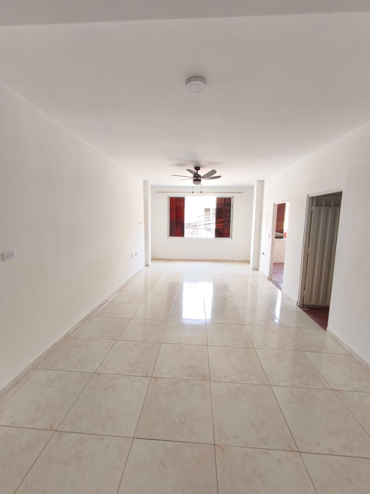 Una gran habitación vacía con suelo de baldosas y un ventilador de techo.