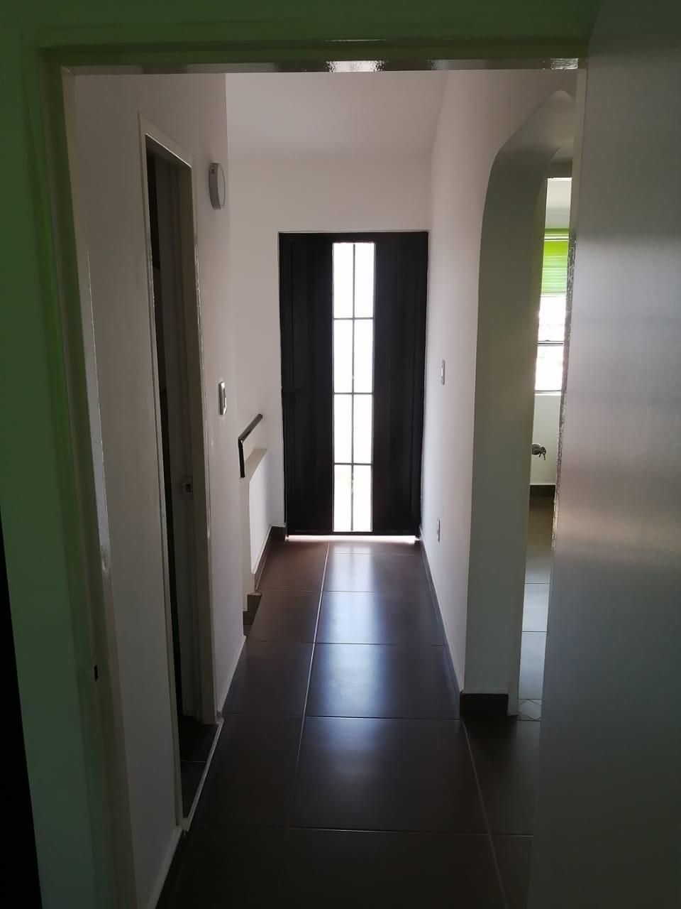 Un pasillo con una puerta negra y una ventana.