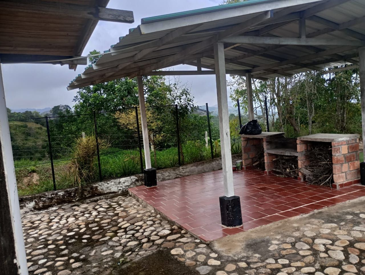Un patio de piedra con una zona cubierta y una valla al fondo.