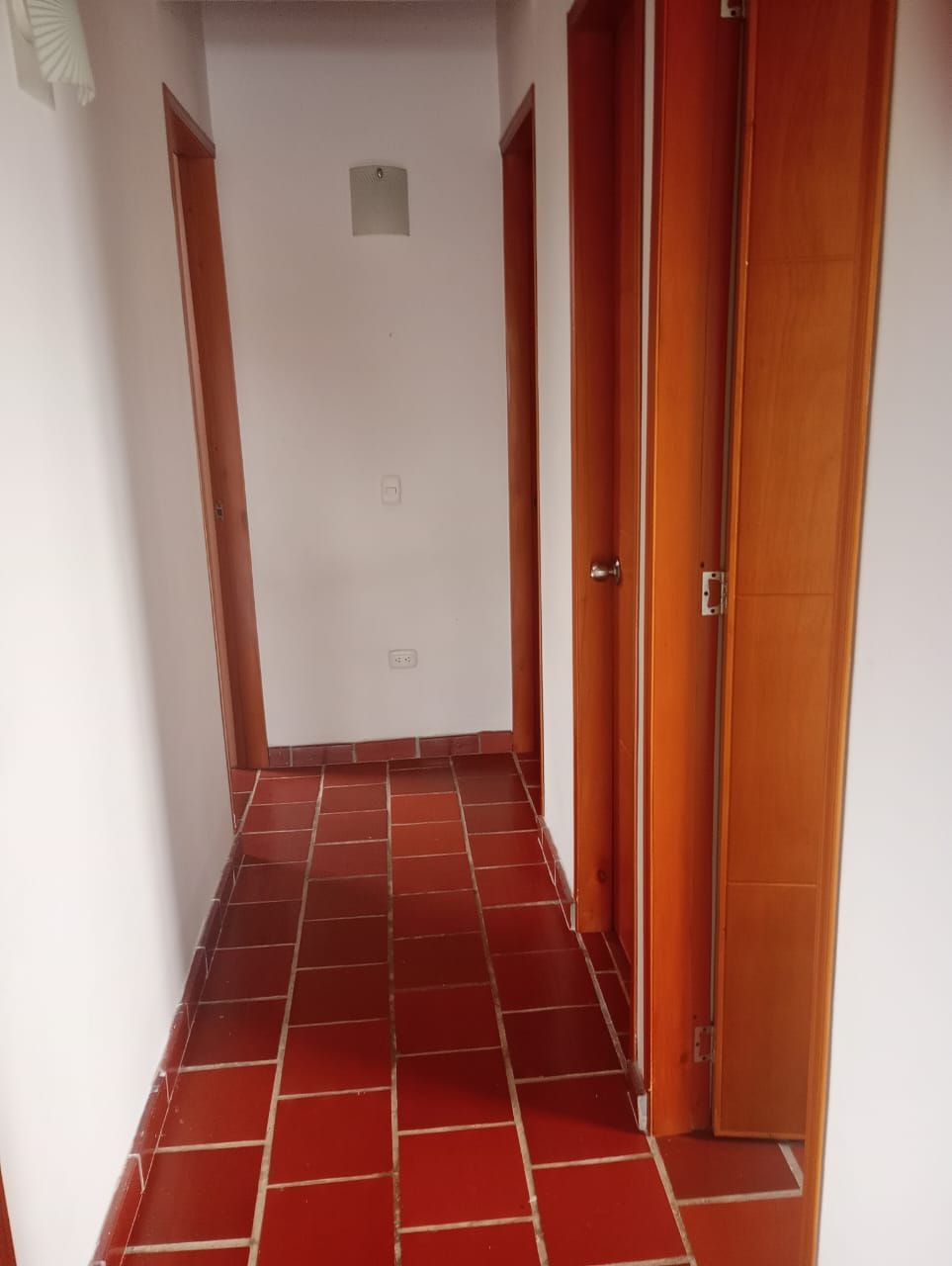 Un pasillo con suelos de baldosas rojas y puertas de madera.