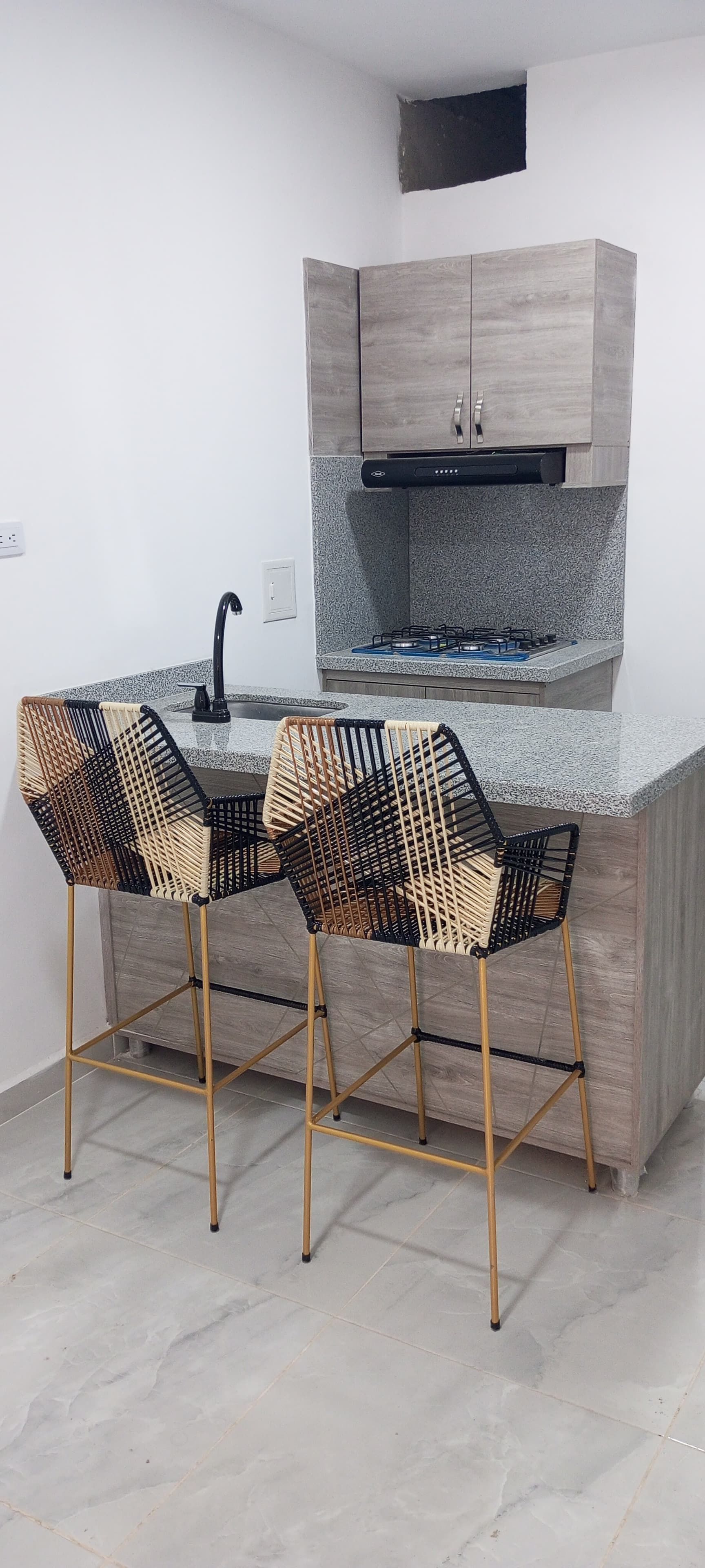 Una cocina con fregadero, estufa y tres taburetes de bar.