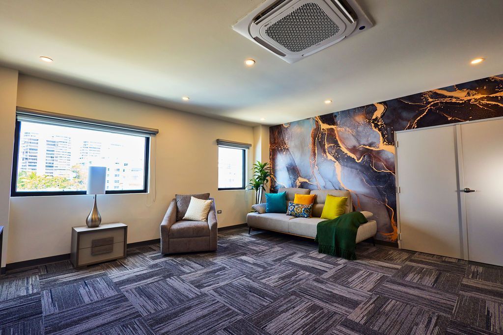 Suite living room at Ola Boutique Hotel with a sofa, an armchair, windows and a dark black and gold feature wall