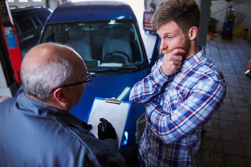 A Man Is Talking To A Mechanic In Front Of A Blue Car — Nuron Inspection & Service Centre In Broadmeadow, NSW