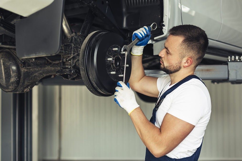 A Man Is Working On The Brake System Of A Car On A Lift — Nuron Inspection & Service Centre In Broadmeadow, NSW