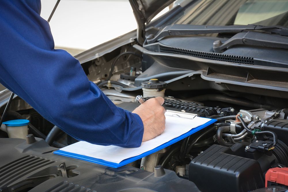 A Mechanic Is Writing On A Clipboard While Working On A Car — Nuron Inspection & Service Centre In Broadmeadow, NSW