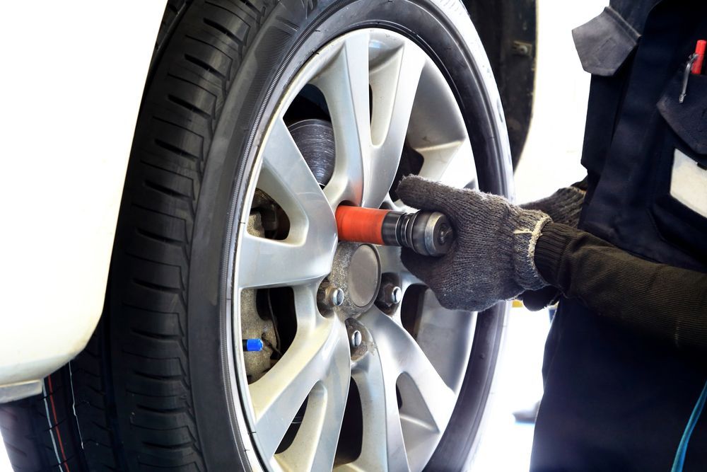 A Person Is Changing A Tire On A Car With A Wrench — Nuron Inspection & Service Centre In Broadmeadow, NSW