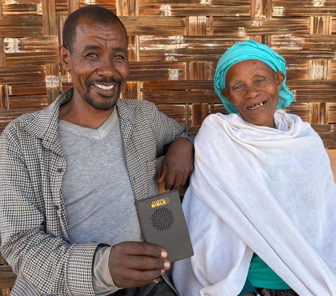 Pastor holding a Talking Bible with lady that used to throw rocks at him. Now they are friends