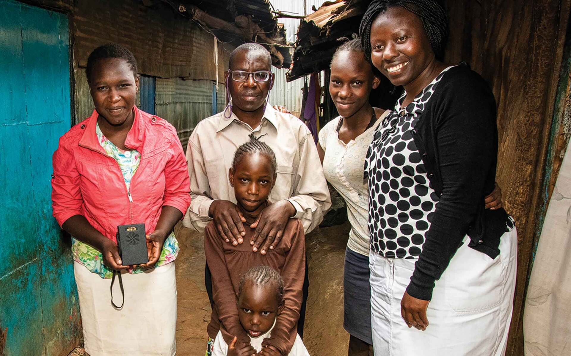 Group of five people standing together in a doorway, smiling at the camera. One is holding a Talking Bible