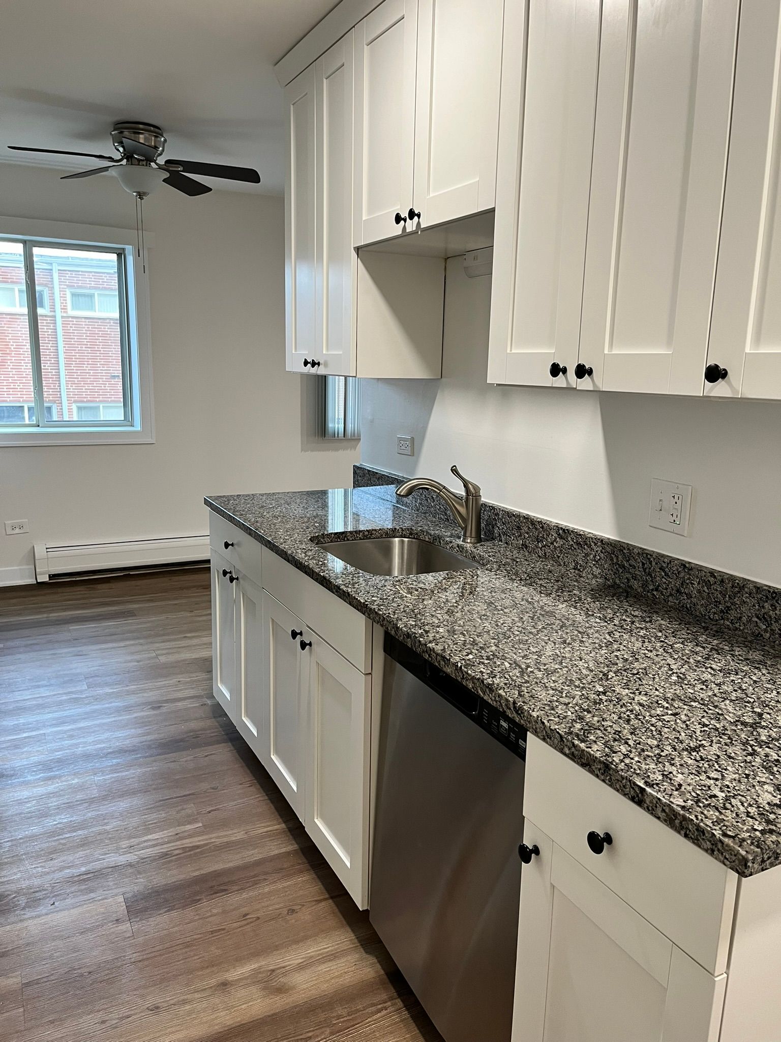 A kitchen with granite counter tops , white cabinets and a stainless steel dishwasher.
