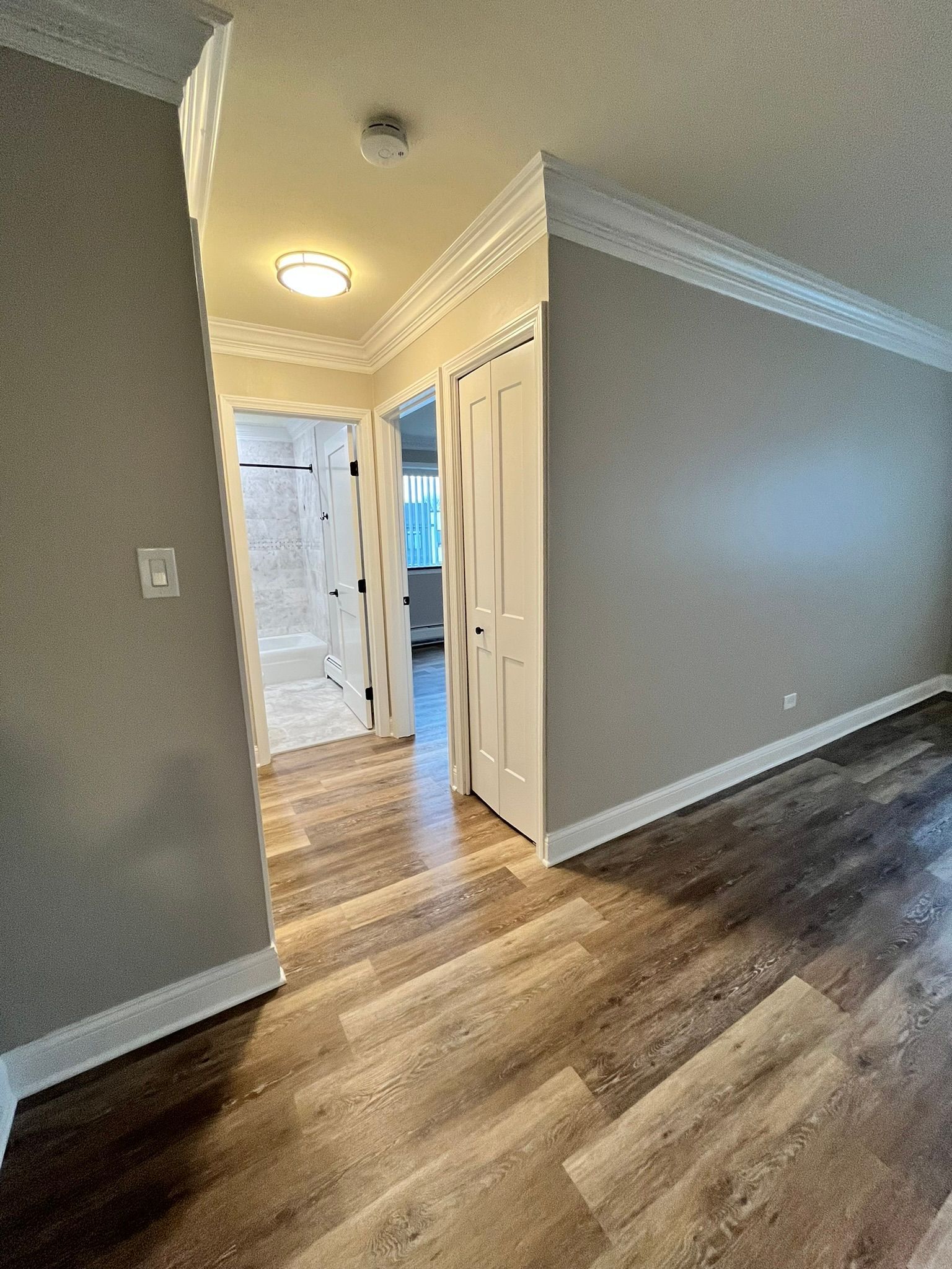 A hallway in a house with hardwood floors leading to a bathroom.