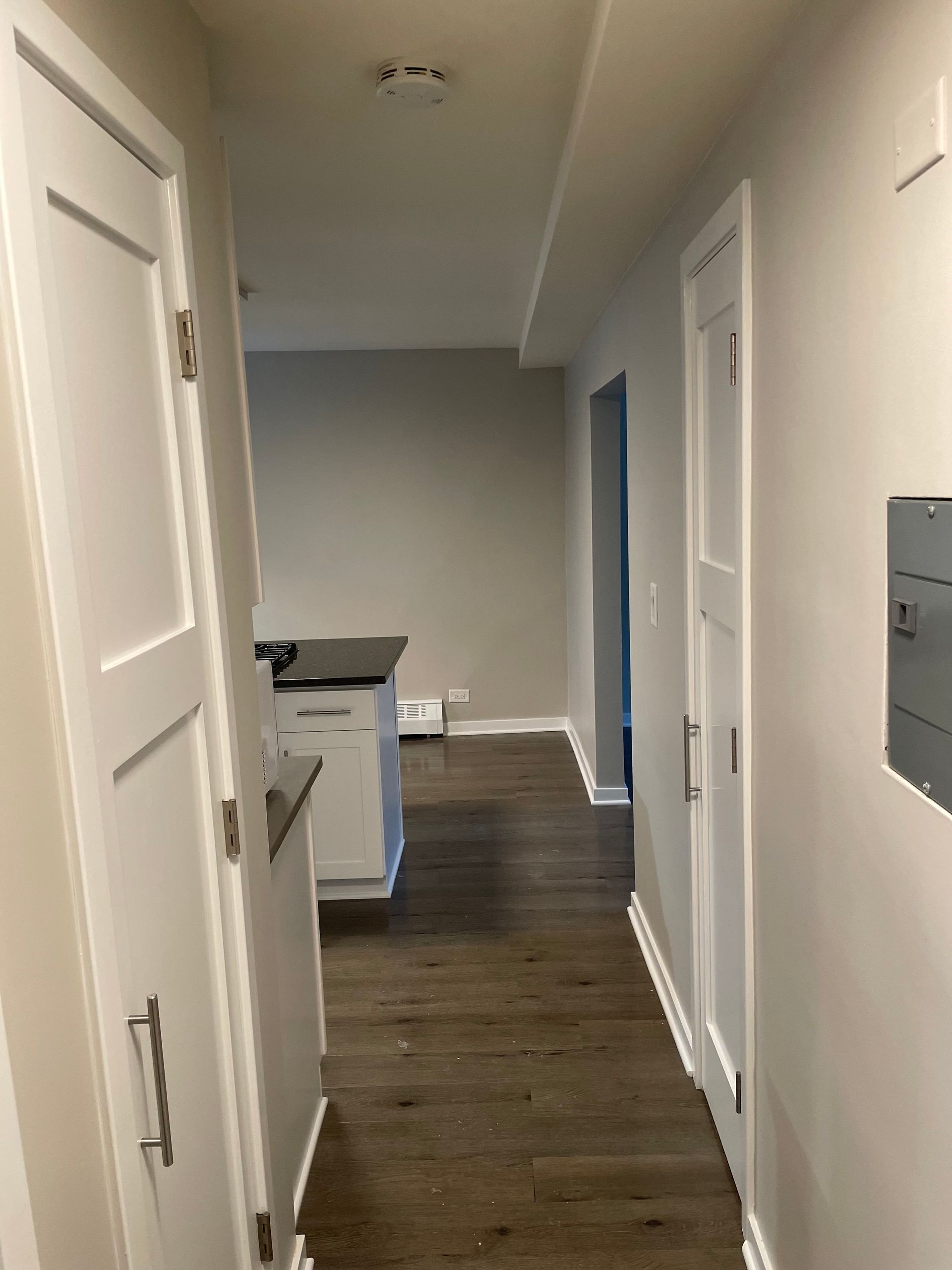 a hallway in a house with wooden floors and white doors leading to a kitchen .