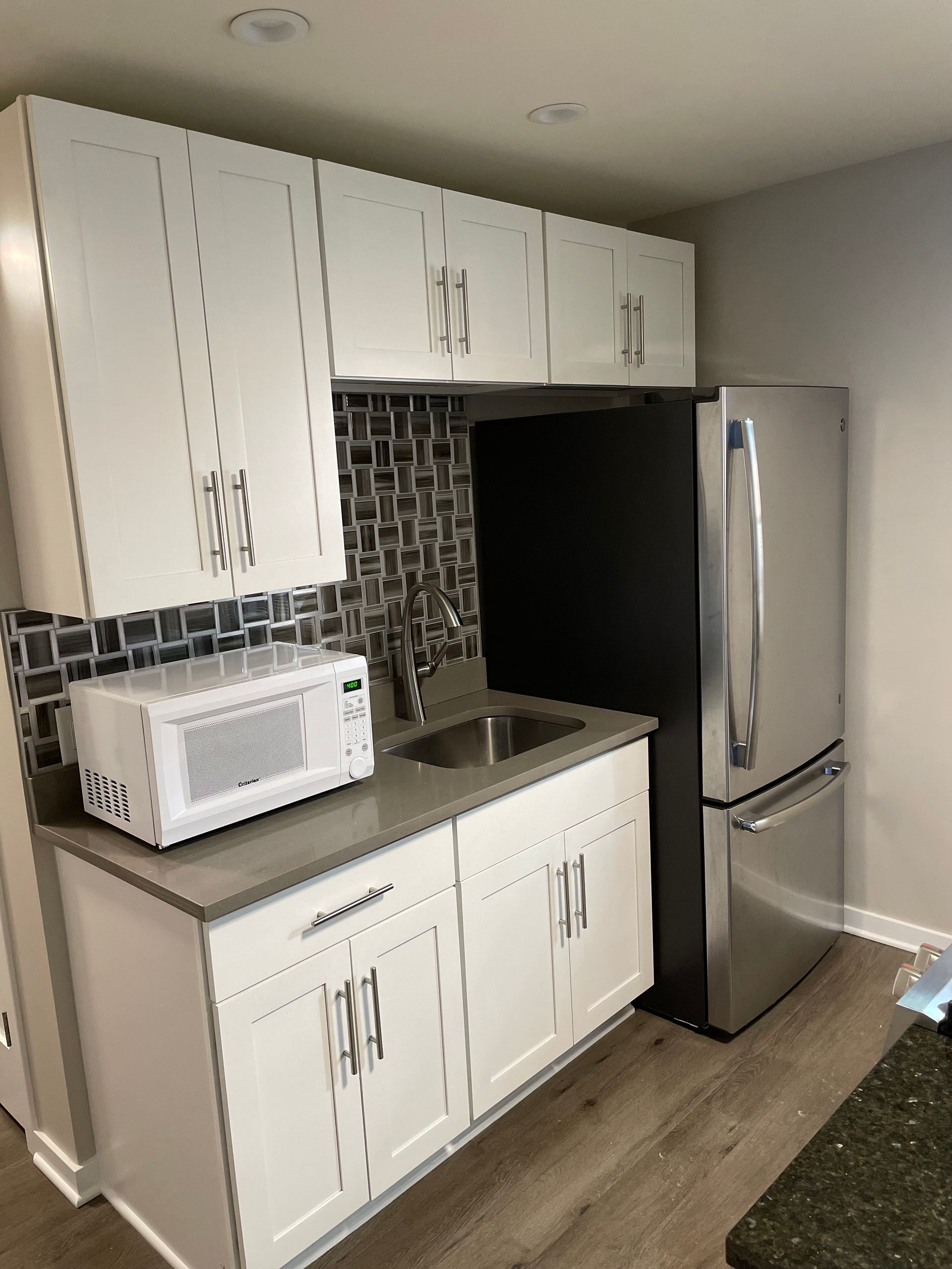 a kitchen with white cabinets , a stainless steel refrigerator , a sink , and a microwave .