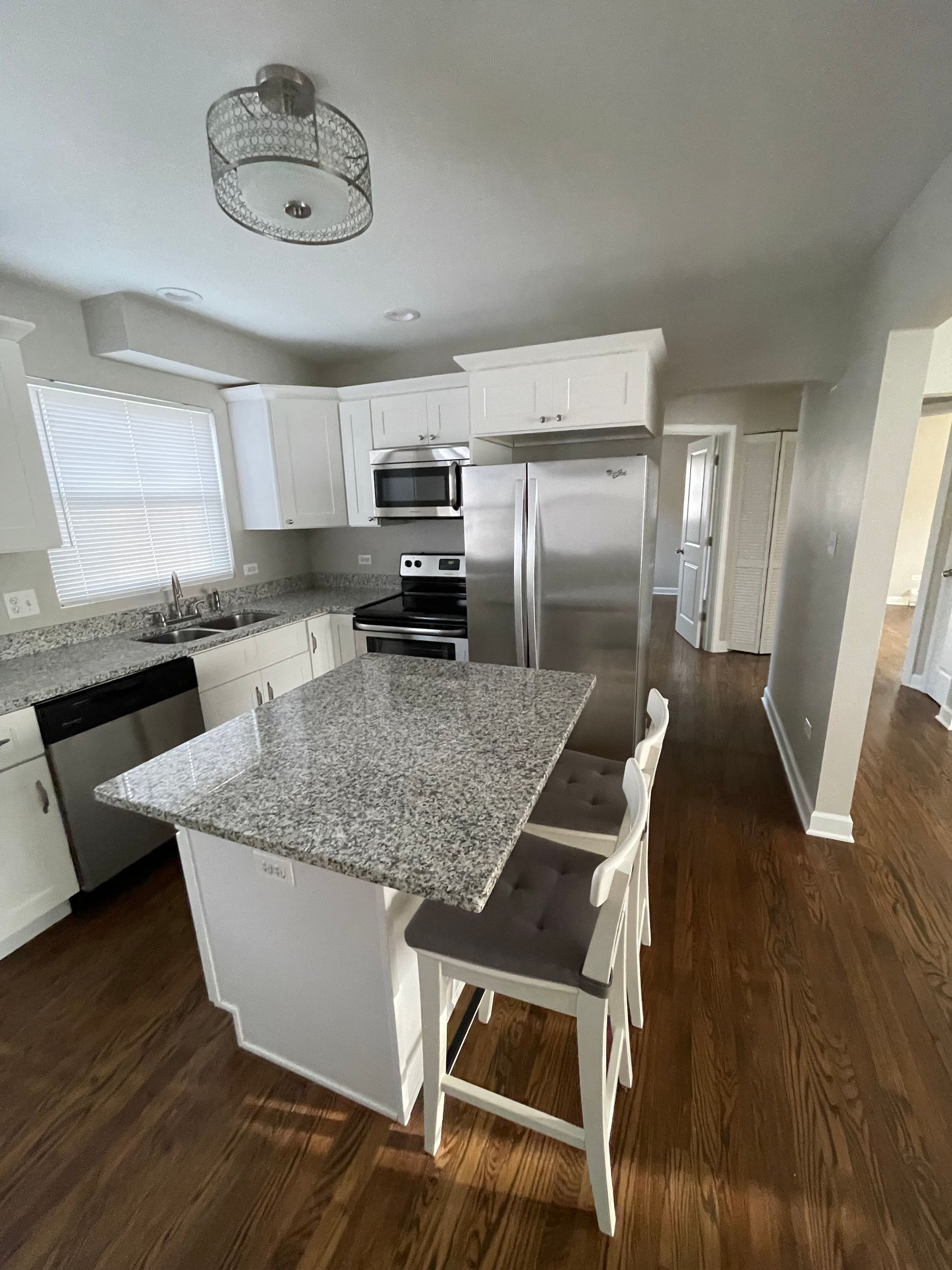 a kitchen with granite counter tops , stainless steel appliances , white cabinets and hardwood floors .