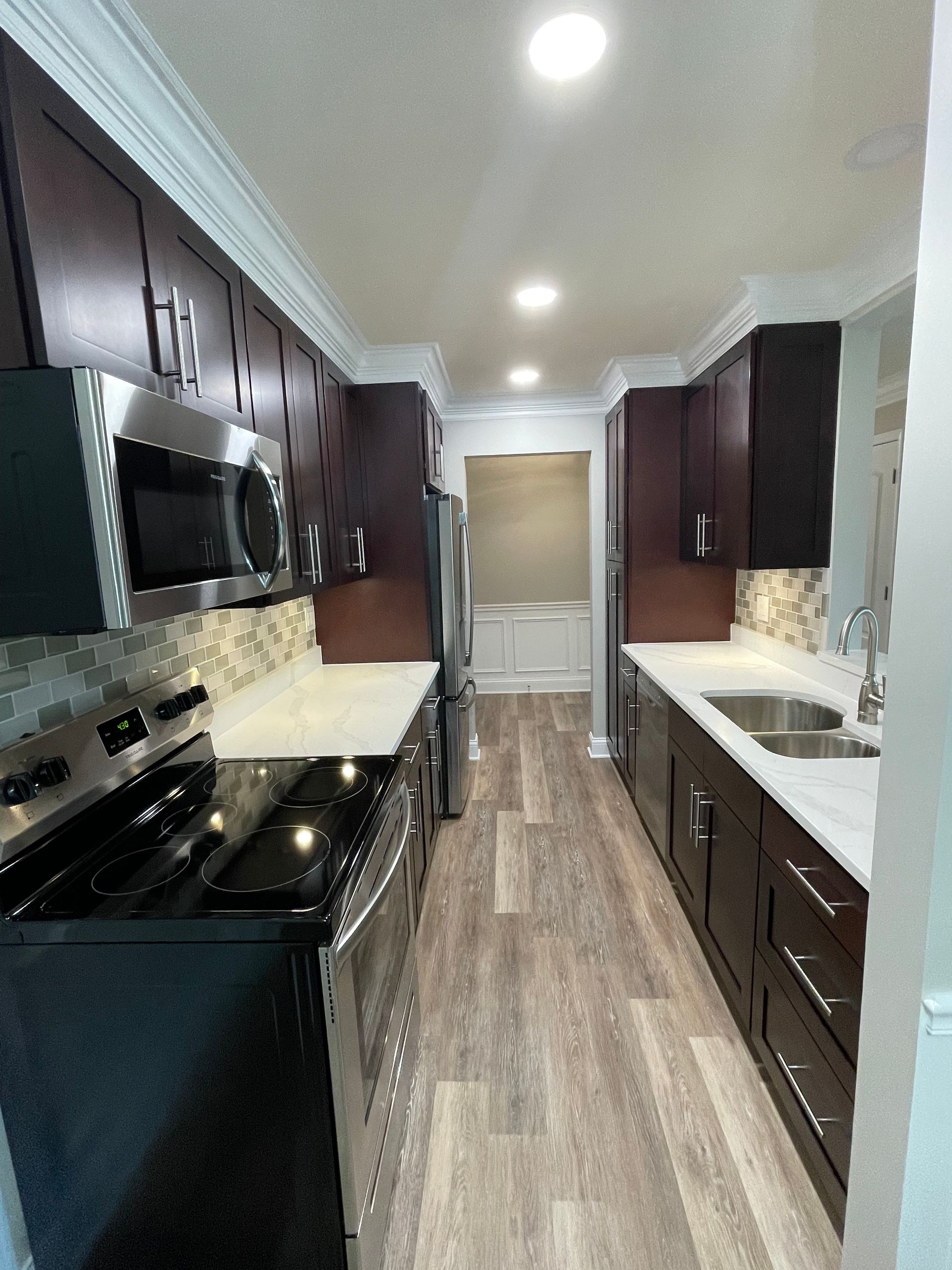 a long kitchen with stainless steel appliances and wooden floors .