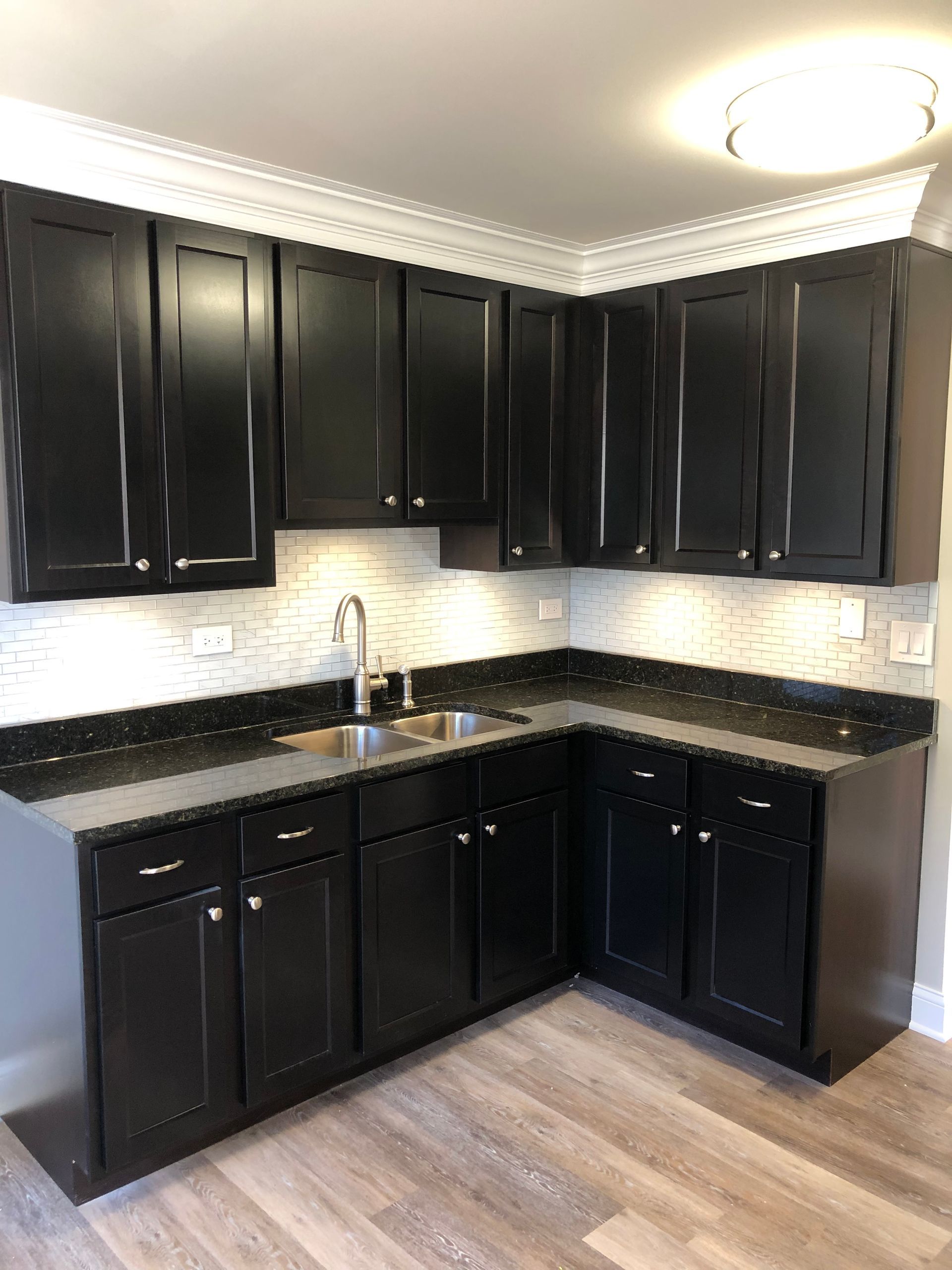 a kitchen with black cabinets , granite counter tops , and a sink .