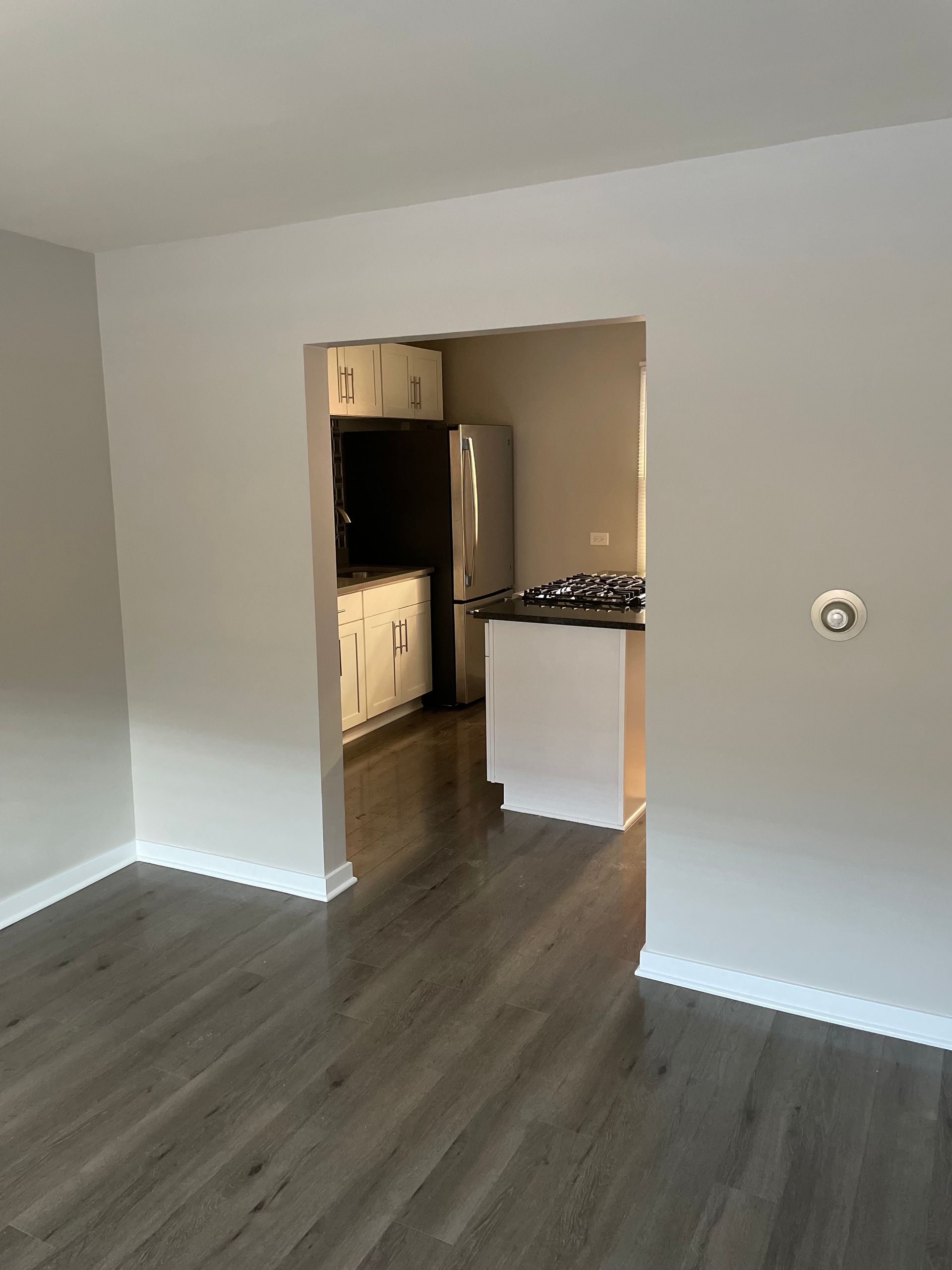 a living room with hardwood floors and a kitchen in the background .