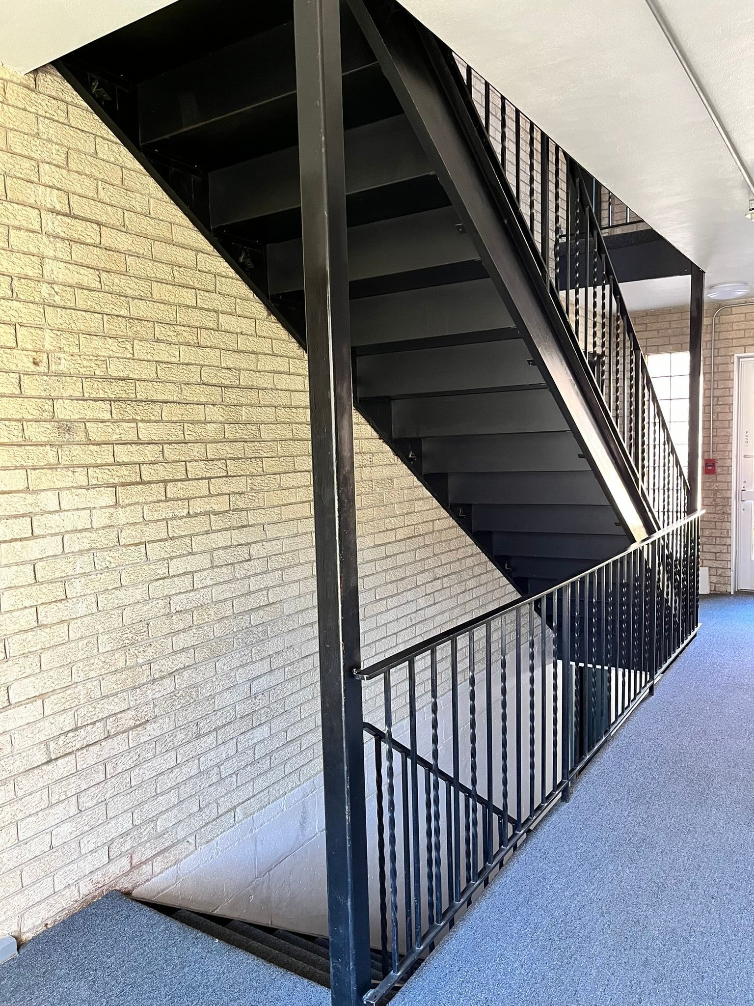 a black staircase with a metal railing in a hallway next to a brick wall .