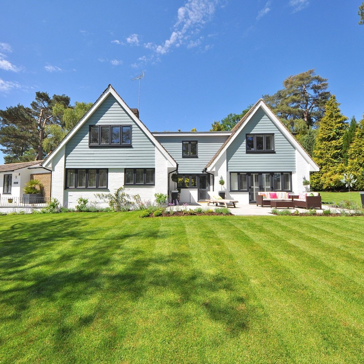 Two-story house with light blue siding and a well-manicured lawn under a blue sky.
