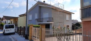 Casa beige a due piani con balcone e cortile recintato, situata in una stretta via residenziale.