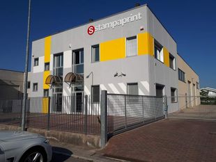 Moderno edificio per uffici a due piani con pannelli bianchi e gialli, situato dietro una recinzione in una strada soleggiata.