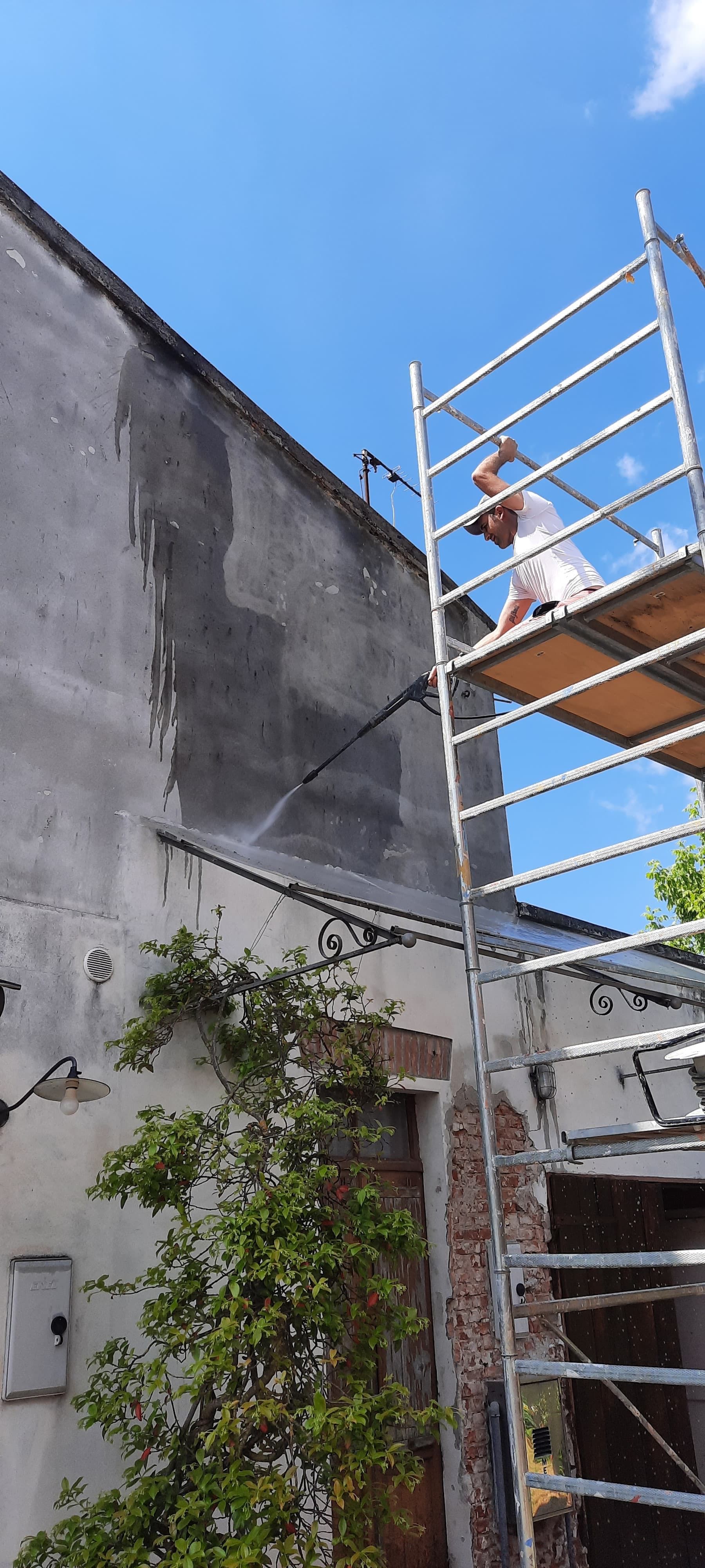 Una persona su un'impalcatura metallica accanto a un muro grigio sotto un cielo blu.