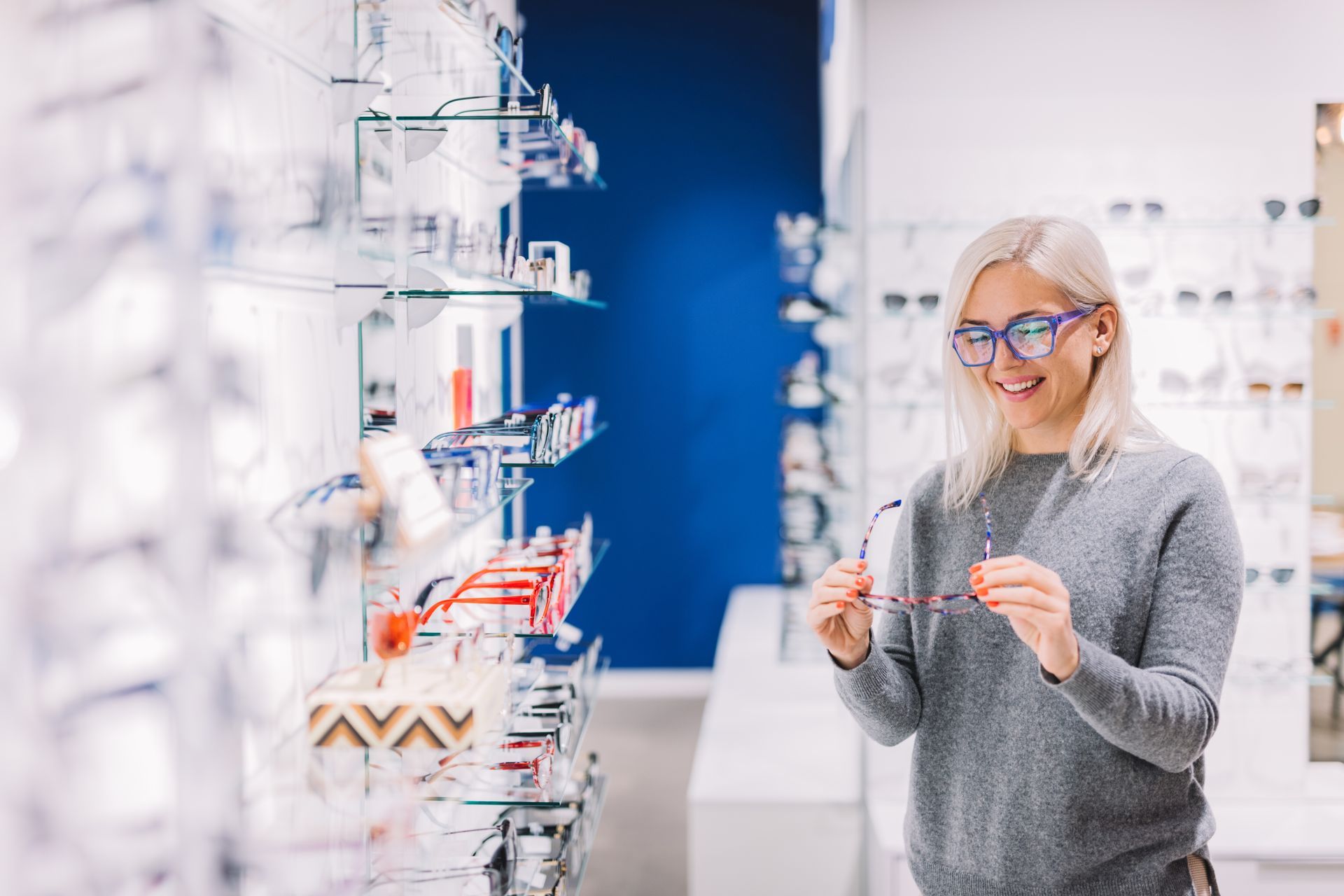 Person browsing eyeglass frames and holding a pair in an optical store.